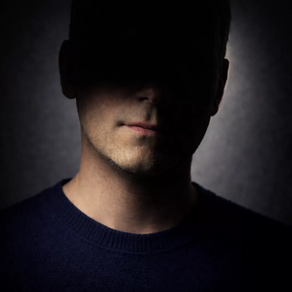 “Portrait of the author Robert Shadow in half-shadow, face partially hidden in darkness against a dark background.”